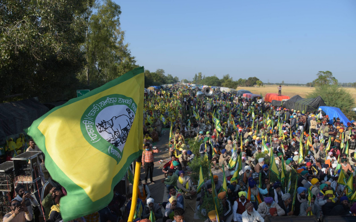 Eine große Menschenmenge mit grünen und gelben Fahnen versammelt sich bei einer Protestveranstaltung auf einer Landstraße.