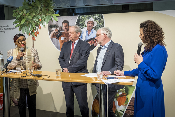 Vier Personen diskutieren angeregt bei einer Podiumsdiskussion vor einem Hintergrund mit landwirtschaftlichen Motiven.