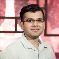 Ein Mann mit Brille lächelt vor einem stilvollen, roten Hintergrund in die Kamera.