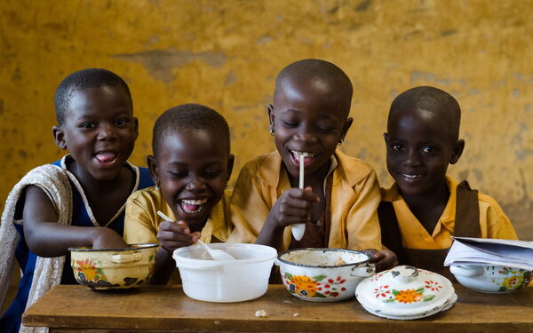 Vier fröhliche Kinder in Schuluniformen genießen gemeinsam eine Mahlzeit an einem Holztisch.