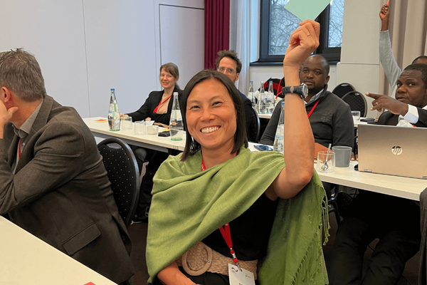 Eine lächelnde Frau hebt in einem Konferenzraum die Hand, während sie an einer Diskussion teilnimmt.