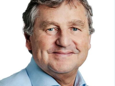 A smiling man with gray hair and a blue shirt poses against a white background.