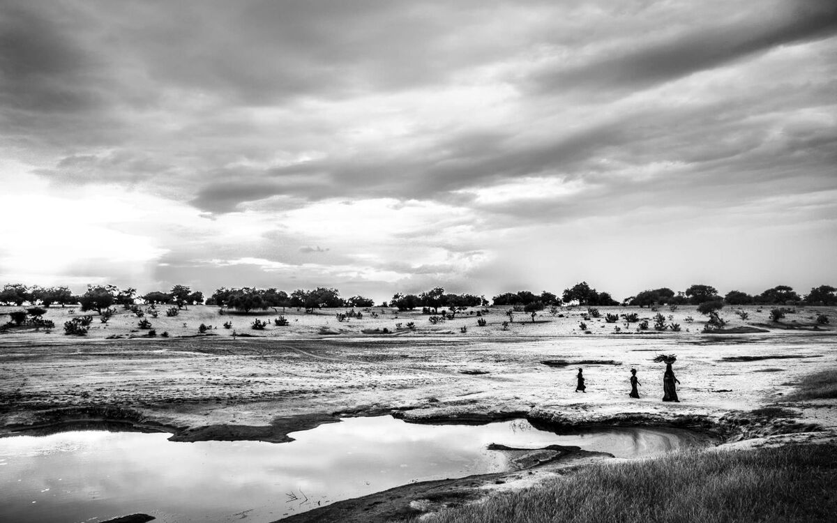 Drei Personen gehen entlang eines ausgetrockneten Sees in einer weiten Landschaft unter dramatisch bewölktem Himmel.