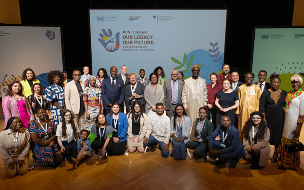 Eine vielfältige Gruppe von Menschen posiert auf einer Bühne vor einem Banner mit der Aufschrift "Unser Erbe, Unsere Zukunft".