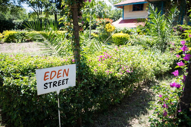 Ein Schild mit der Aufschrift "Eden Street" steht in einem blühenden Garten vor einem Haus.