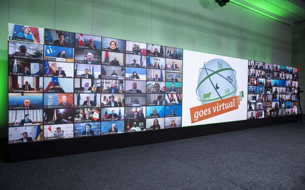 Eine große Videowand zeigt Teilnehmer bei einer virtuellen Konferenz mit dem Slogan "goes virtual".