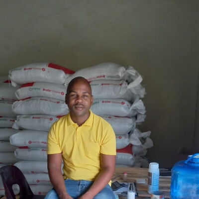 Ein Mann in gelbem T-Shirt sitzt auf Paletten vor gestapelten Säcken in einem Lagerraum.