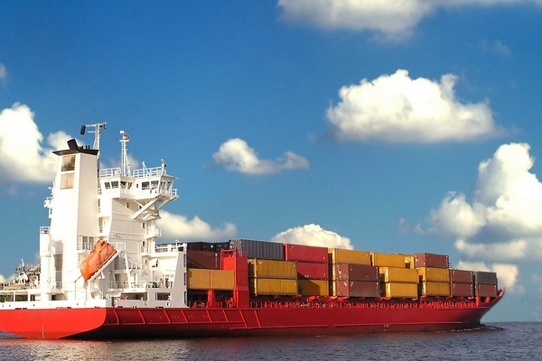 Ein großes Containerschiff mit bunten Frachtboxen fährt unter einem klaren blauen Himmel über das Meer.