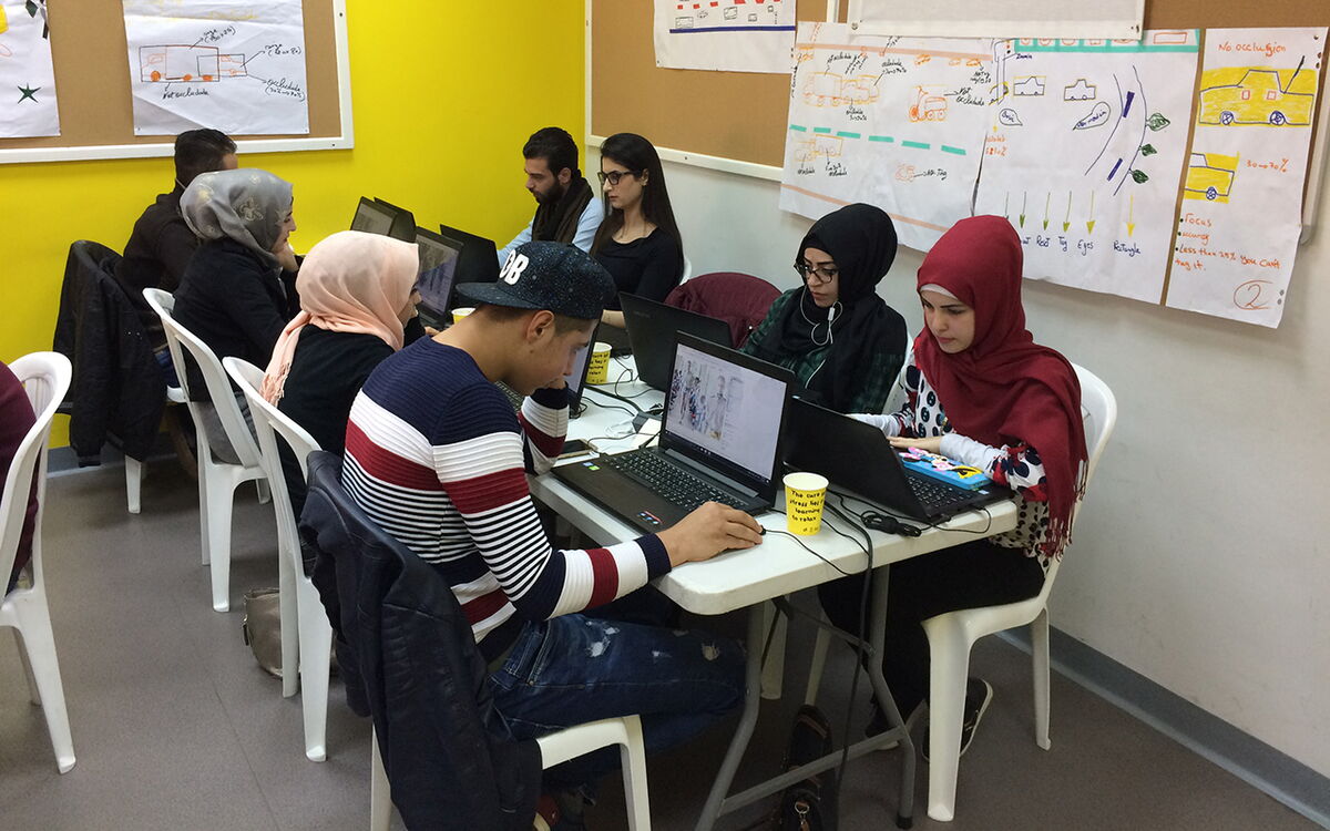 Eine Gruppe junger Menschen arbeitet konzentriert an Laptops in einem Schulungsraum mit gelben Wänden.