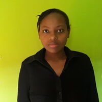 Eine Person in schwarzer Kleidung steht vor einem hellgrünen Hintergrund und schaut direkt in die Kamera.