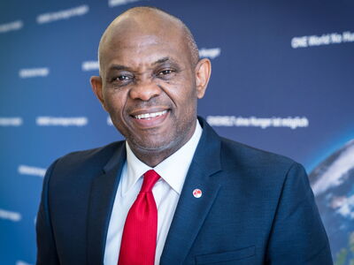 Ein Mann im Anzug lächelt bei der GiZ-Konferenz vor einem dunkelblauen Hintergrund mit unscharfem Text.