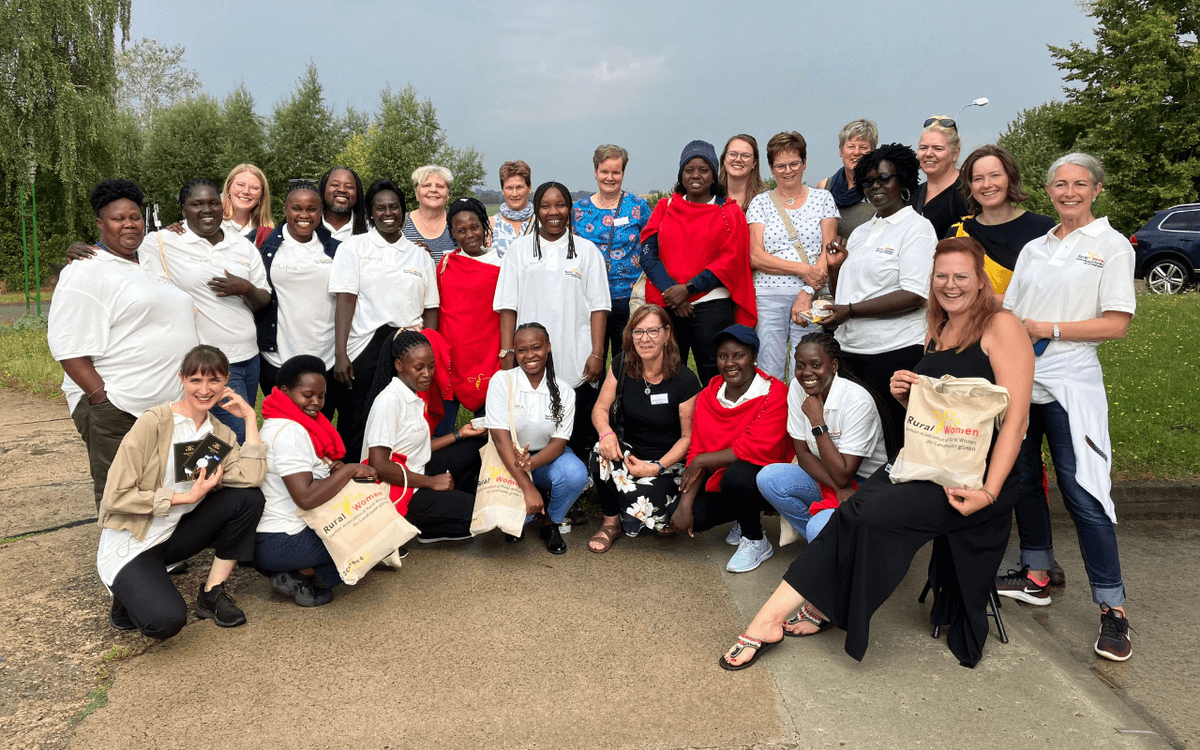 Eine Gruppe von Frauen posiert fröhlich im Freien für ein Gruppenfoto, einige tragen Taschen mit der Aufschrift "Rural Women".
