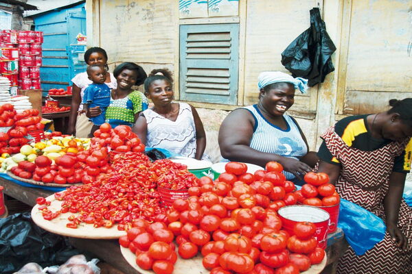 Frauen auf einem Markt in Ghana verkaufen frische Tomaten und Paprika mit einem Lächeln auf den Gesichtern.