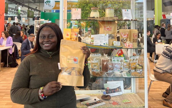 A woman at a trade show proudly displays organic food products in front of a booth showcasing diverse packaged goods.