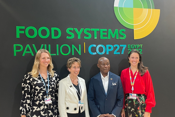 Vier Personen stehen vor dem Schild "Food Systems Pavilion COP27" in Ägypten und lächeln in die Kamera.