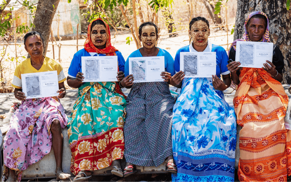 Fünf Frauen in Madagaskar halten stolz ihre Landtitel in der Hand, während sie bunte Kleidung tragen.