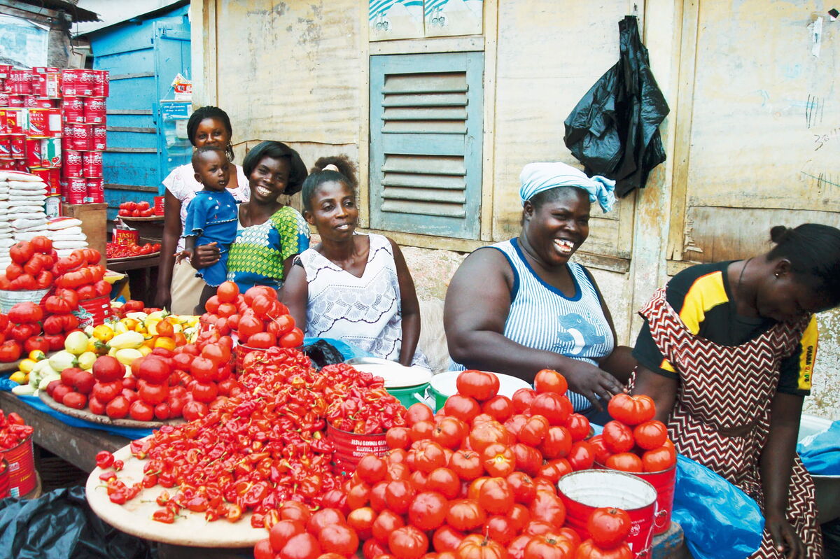 Frauen verkaufen frische Tomaten und Paprika auf einem bunten Marktstand, lächelnd und in geselliger Atmosphäre.