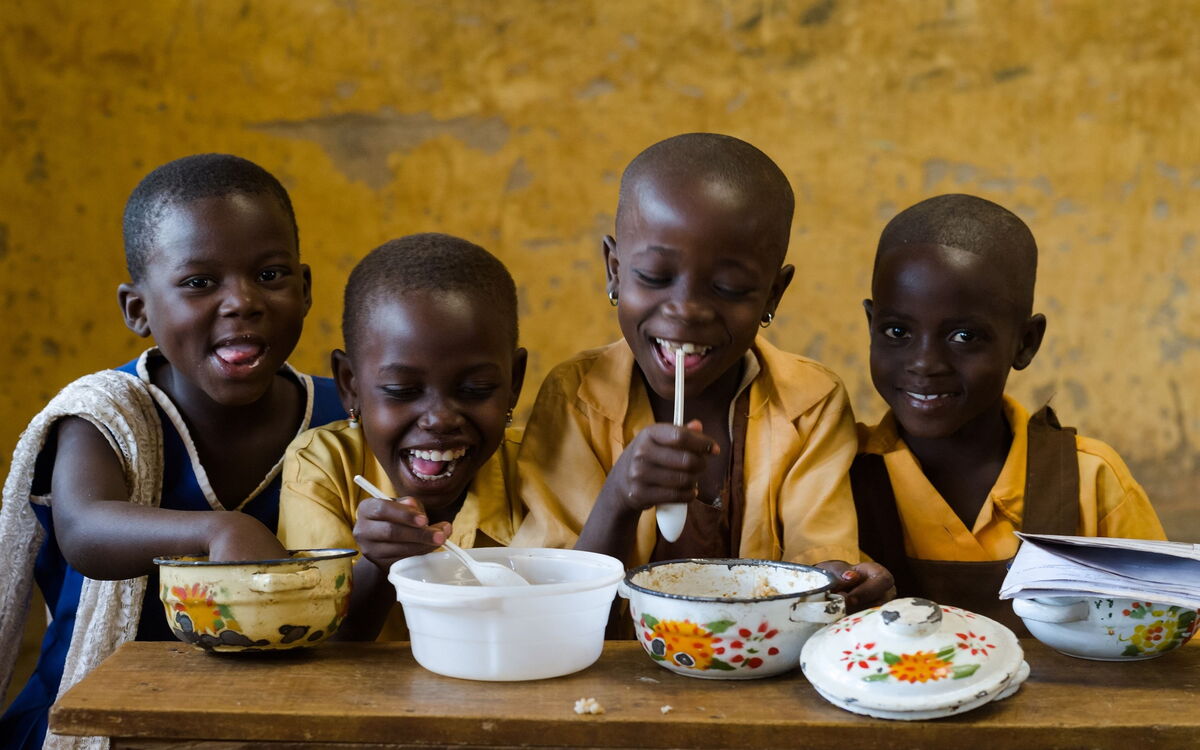 Vier fröhliche Kinder in Schuluniformen genießen gemeinsam eine Mahlzeit an einem Holztisch.