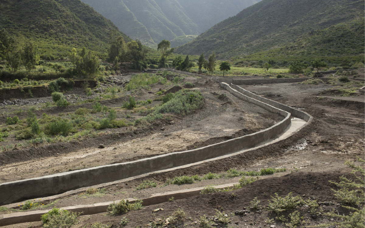 Ein Bewässerungskanal schlängelt sich durch eine hügelige, grüne Landschaft in Äthiopien, umgeben von Bergen.