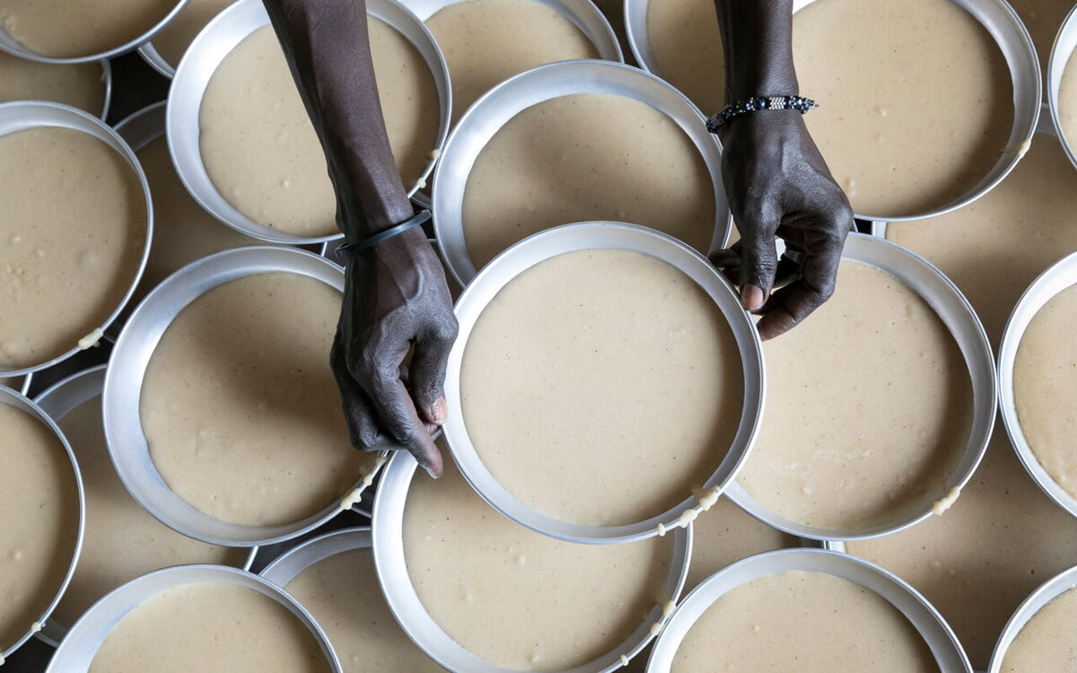 Zwei Hände platzieren Ringe auf gefüllte Backformen, die dicht aneinander gereiht sind.