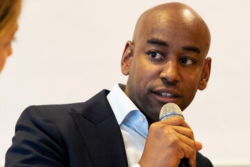 A man in a suit is speaking into a microphone during a discussion at an event.