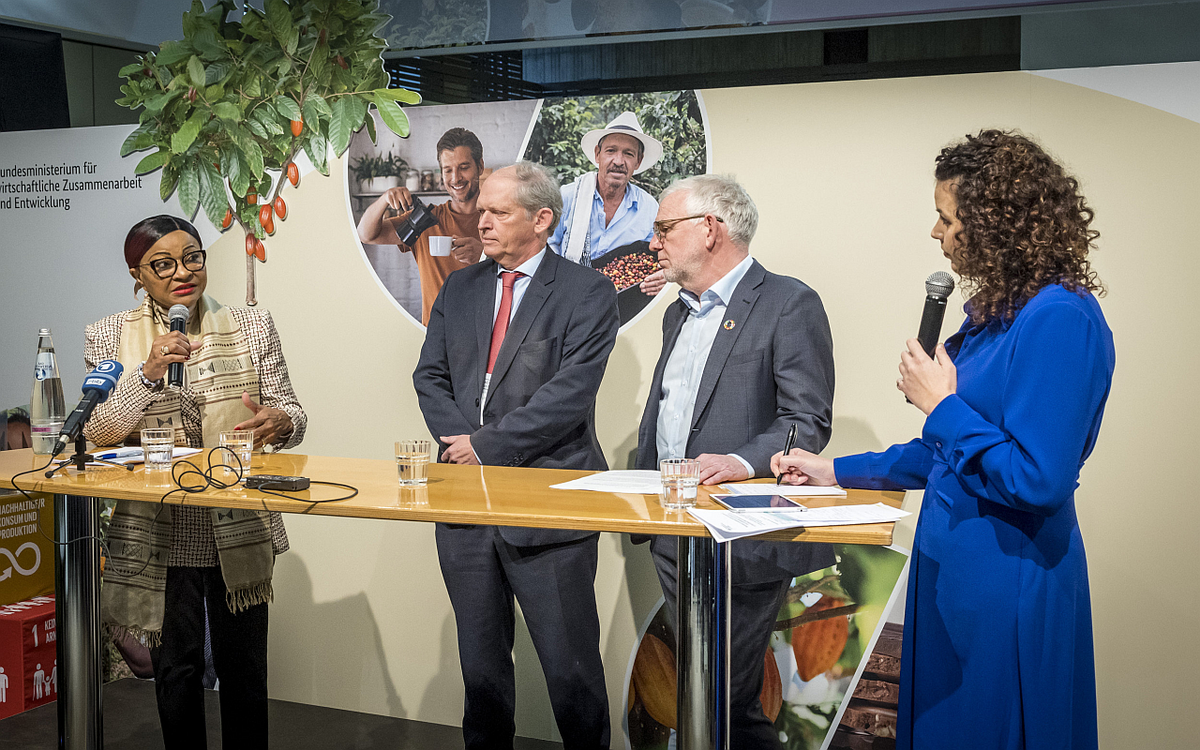 Vier Personen diskutieren angeregt bei einer Podiumsdiskussion vor einem Hintergrund mit landwirtschaftlichen Motiven.