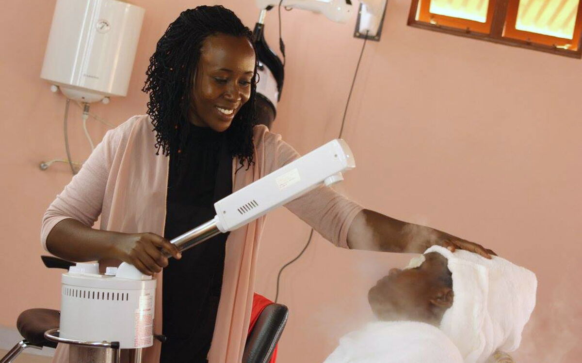 A woman performs a facial steam treatment on a client in a beauty salon in Uganda.