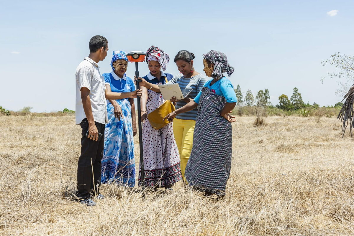 Eine Gruppe von Menschen steht in einem trockenen Feld und betrachtet gemeinsam ein Dokument für ein Projekt.