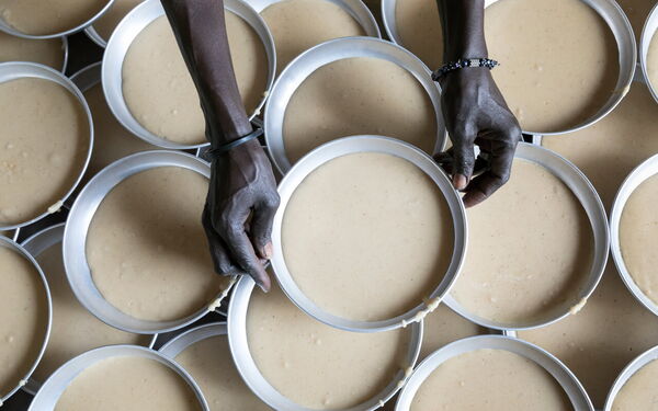 Hands arrange multiple circular molds filled with batter, creating a pattern of preparation and culinary artistry.