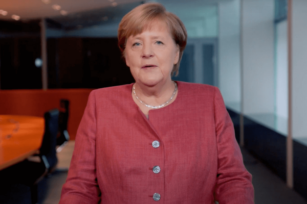Eine Frau in einem roten Blazer steht in einem modernen Konferenzraum und spricht in die Kamera.