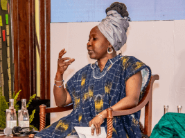 Eine Frau in traditioneller Kleidung spricht engagiert auf einer Podiumsdiskussion.
