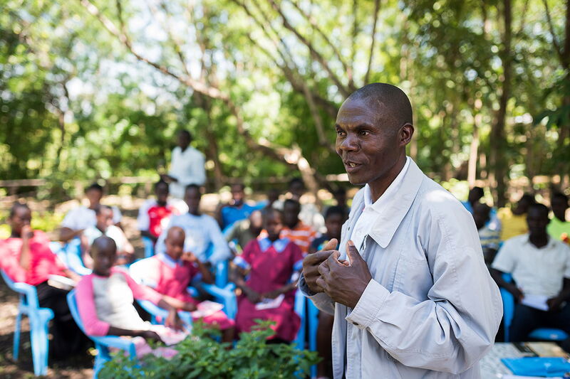 Ein Mann hält im Freien vor einer Gruppe aufmerksamer Zuhörer einen Vortrag.