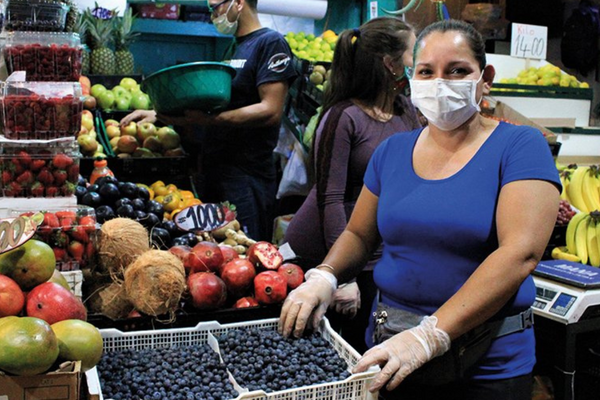 Eine Frau verkauft Blaubeeren auf einem lebhaften Markt, während sie einen Mundschutz und Handschuhe trägt.