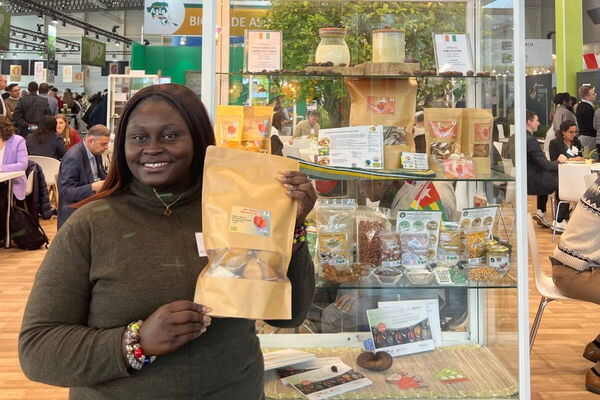 Eine Frau präsentiert auf der BIOFACH-Messe ein Produkt vor einem Regal mit biologischen Lebensmitteln.