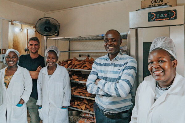 Eine Gruppe von fünf lächelnden Menschen steht in einer Bäckerei neben einer Ladung frischer Backwaren.