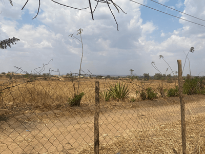 A dry, expansive field is enclosed by a wire fence under a cloudy sky, highlighting the arid landscape.