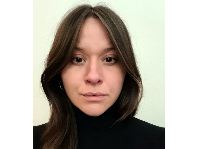 Eine Frau mit langen braunen Haaren trägt einen schwarzen Rollkragenpullover und schaut direkt in die Kamera.