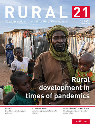 Ein Mann mit Kindern steht vor einem einfachen Gebäude in einer ländlichen Gegend, symbolisiert ländliche Entwicklung.