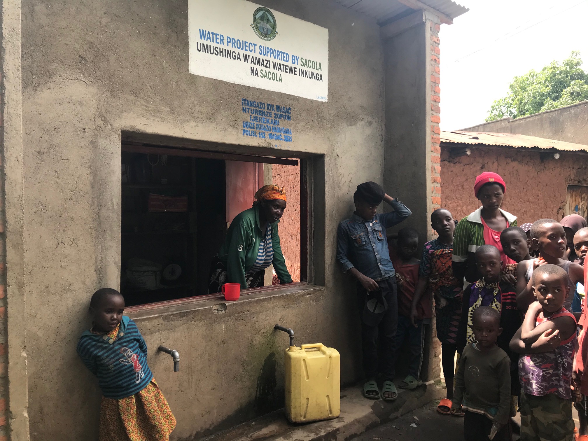 Menschen in Rwanda versammeln sich an einem Wasserprojekt, während ein gelber Kanister Wasser auffängt.