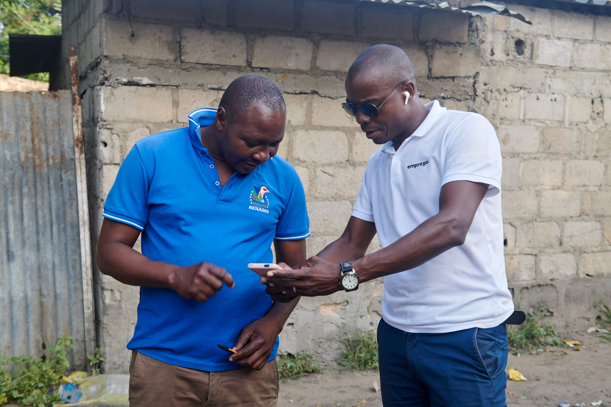 Zwei Männer stehen draußen und schauen gemeinsam auf ein Smartphone, während sie Informationen austauschen.