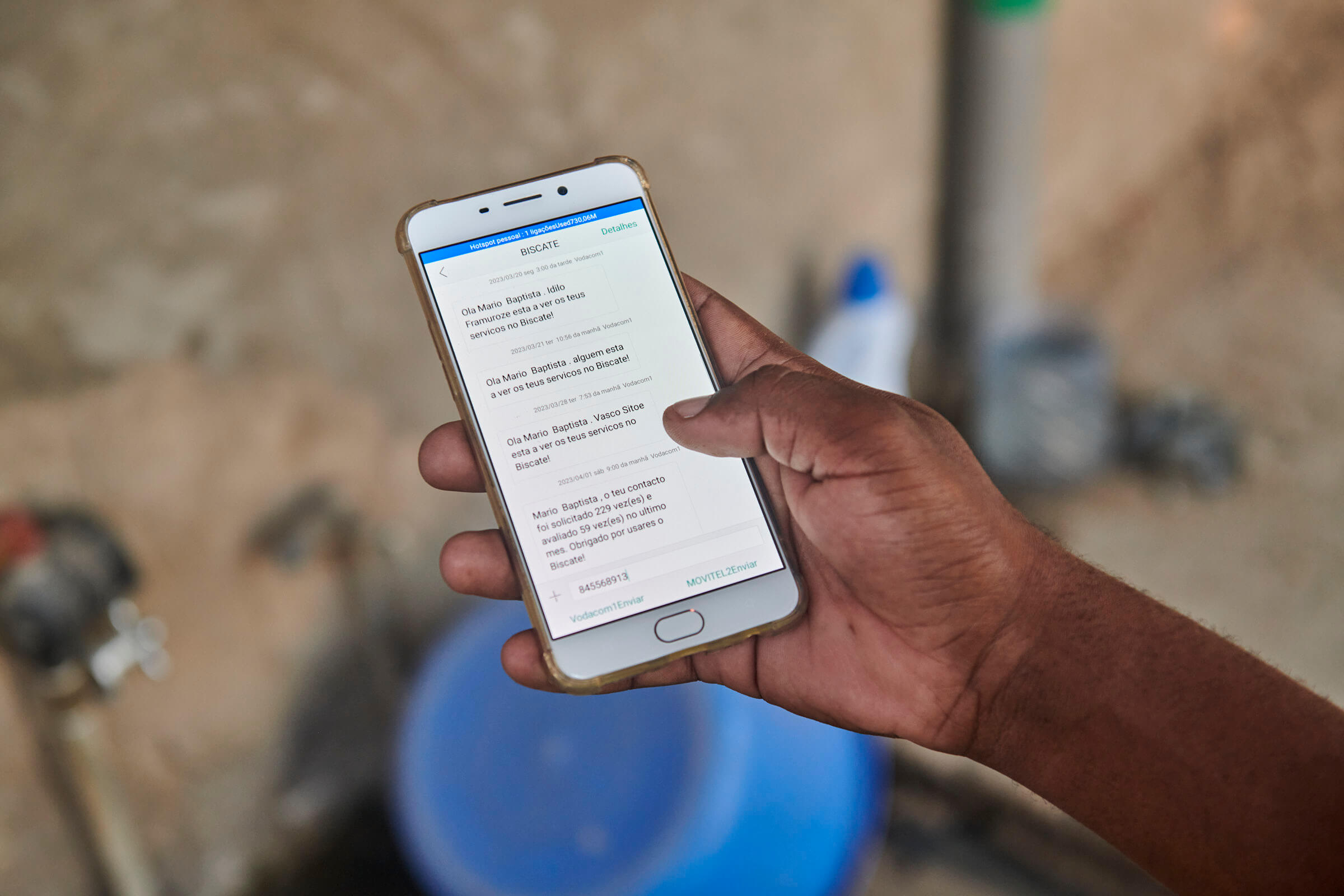 Eine Hand hält ein Smartphone, auf dem SMS-Nachrichten angezeigt werden, die Arbeiter über Kundenanfragen informieren.