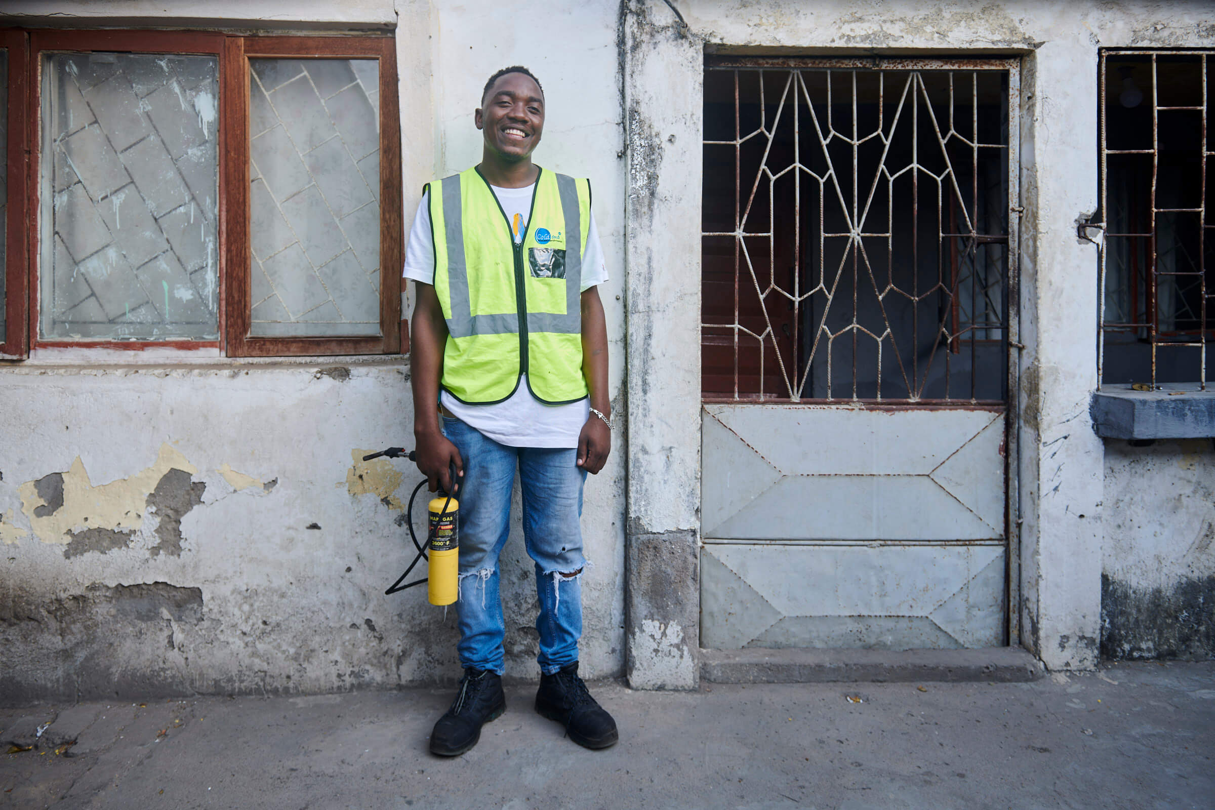 Ein Mann in Warnweste steht lächelnd mit einem Sprühgerät vor einem alten Gebäude, bereit für die Arbeit.