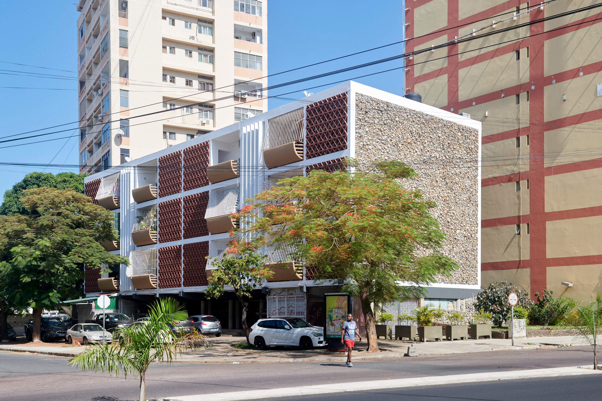 Ein modernes Gebäude in Maputo, Mosambik, mit markanter Fassade und Bäumen, ist von einer belebten Straße umgeben.