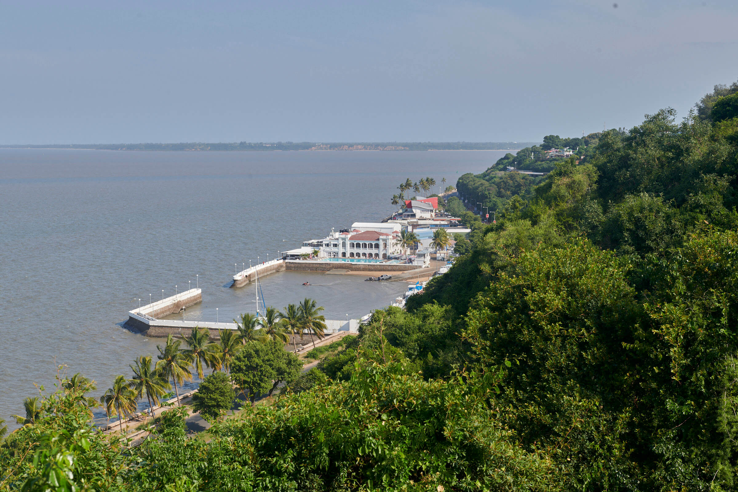 Blick auf den Hafen von Maputo am Indischen Ozean, umgeben von üppigem Grün und Palmen.