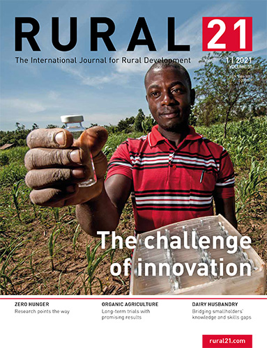 A man in a striped shirt holds a vial in a field, embodying rural innovation and development themes.