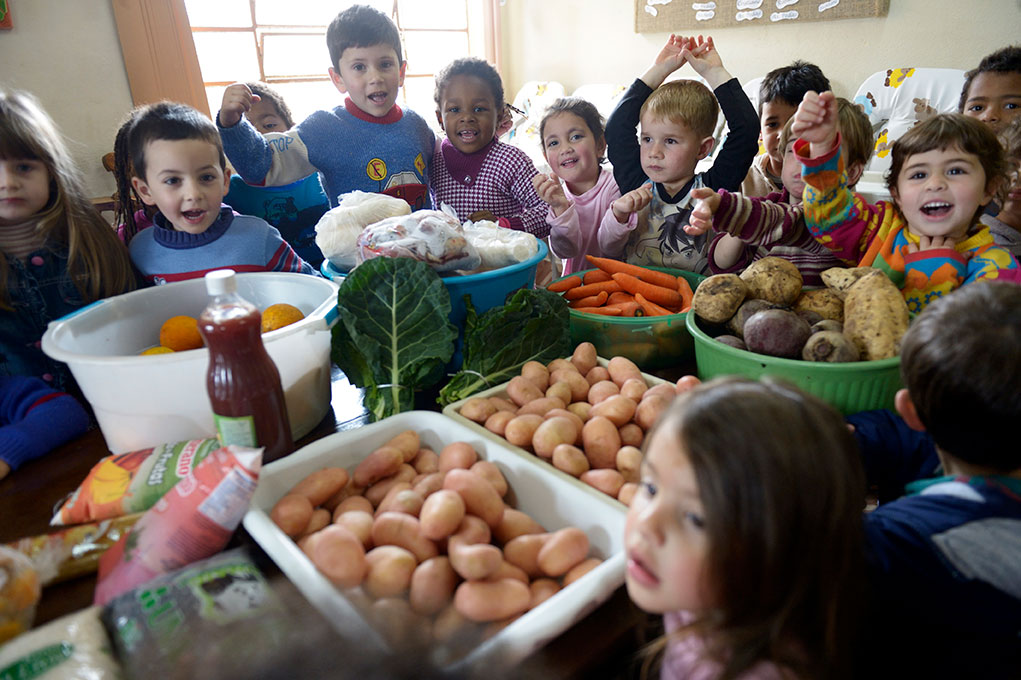 Eine Gruppe fröhlicher Kinder sitzt um einen Tisch voller frischer Lebensmittel wie Kartoffeln und Karotten.
