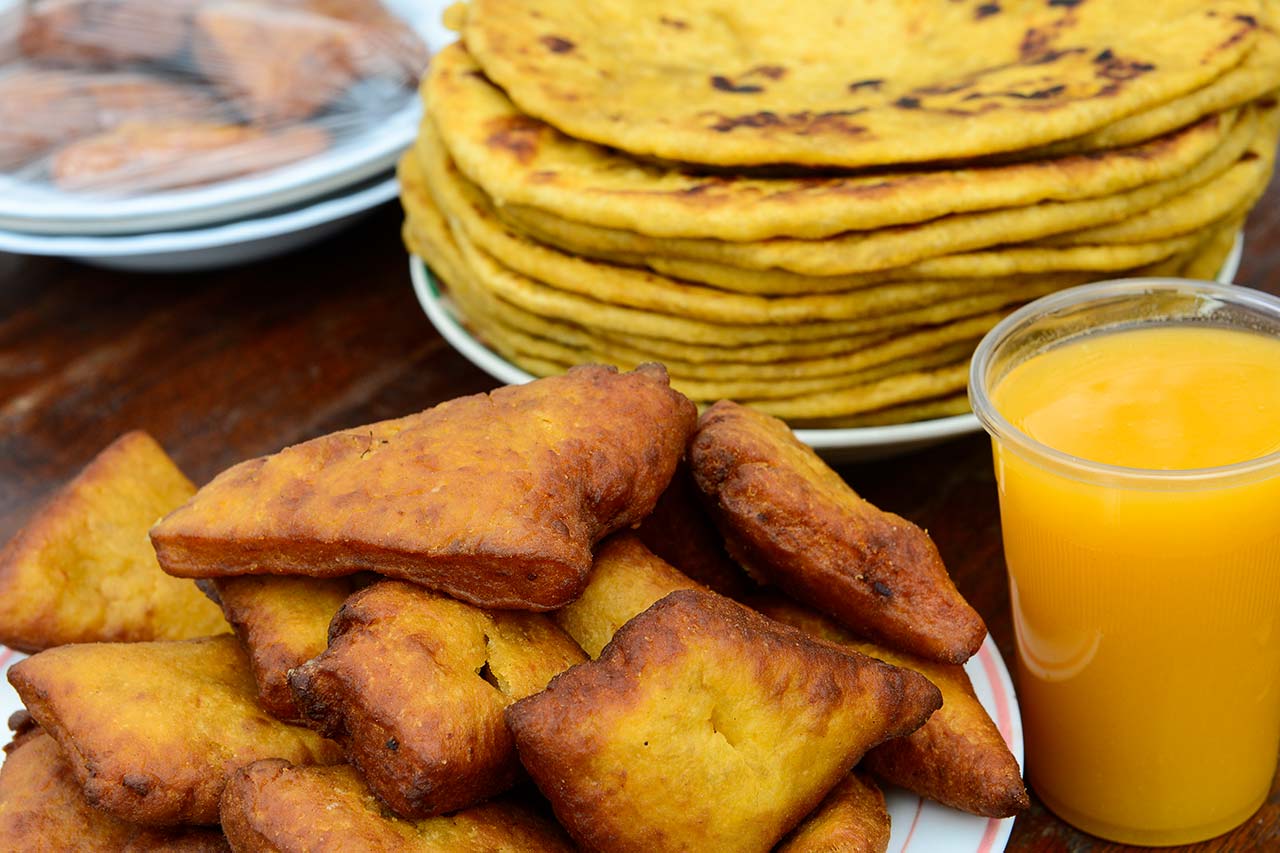 A plate of Kenyan mandazi and chapati is served with a glass of fresh orange juice on a wooden table.